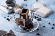 Coffee filter being used to brew coffee in a glass cup with coffee beans around on surface.